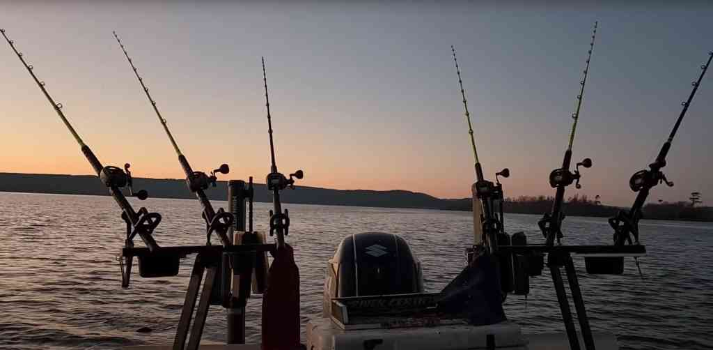 Six fishing rods, including bright Hellcats, arrayed at the stern of a boat with a sunset backdrop.